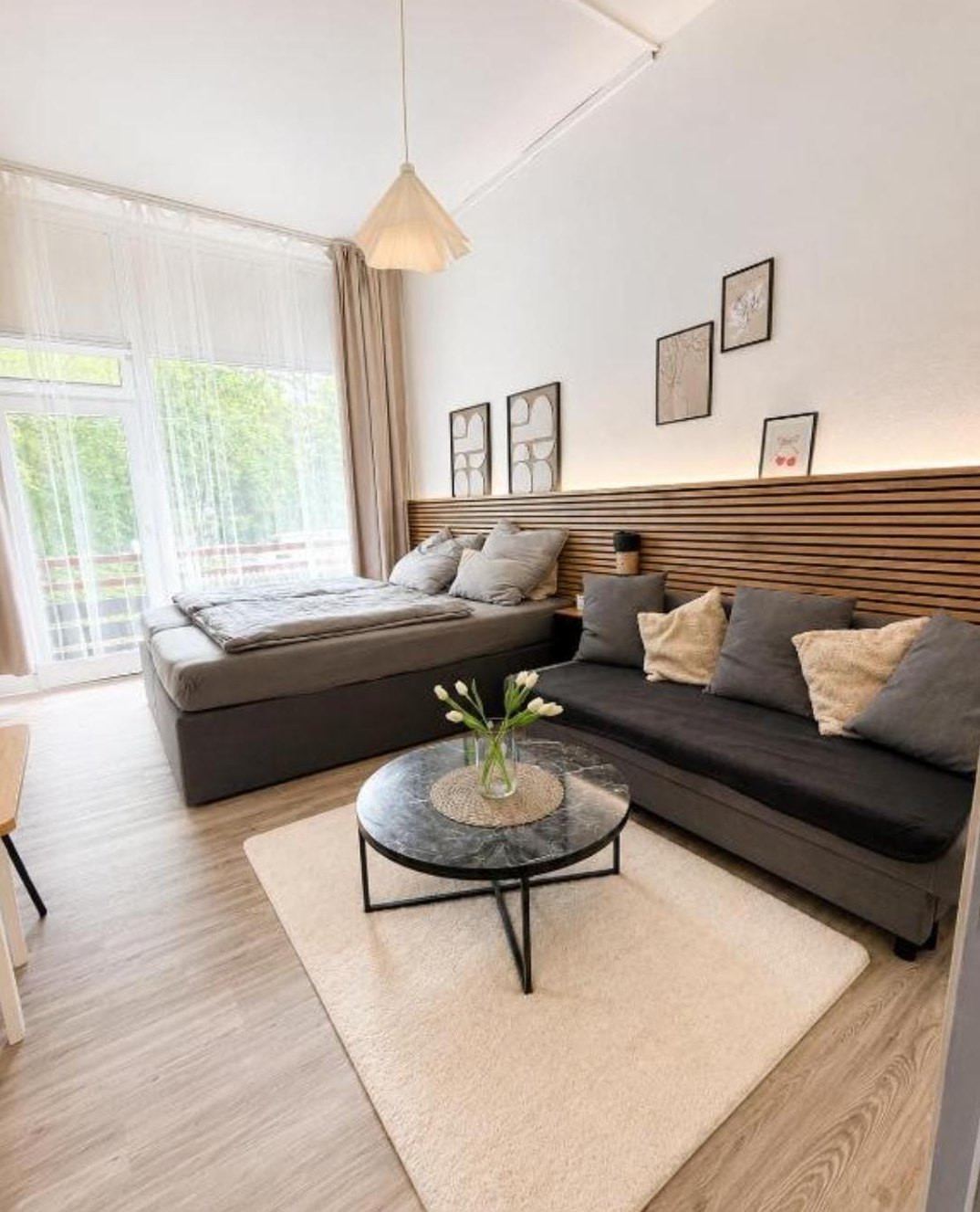 Heller Wohnraum mit großem Fenster, Doppelbett und Sofa